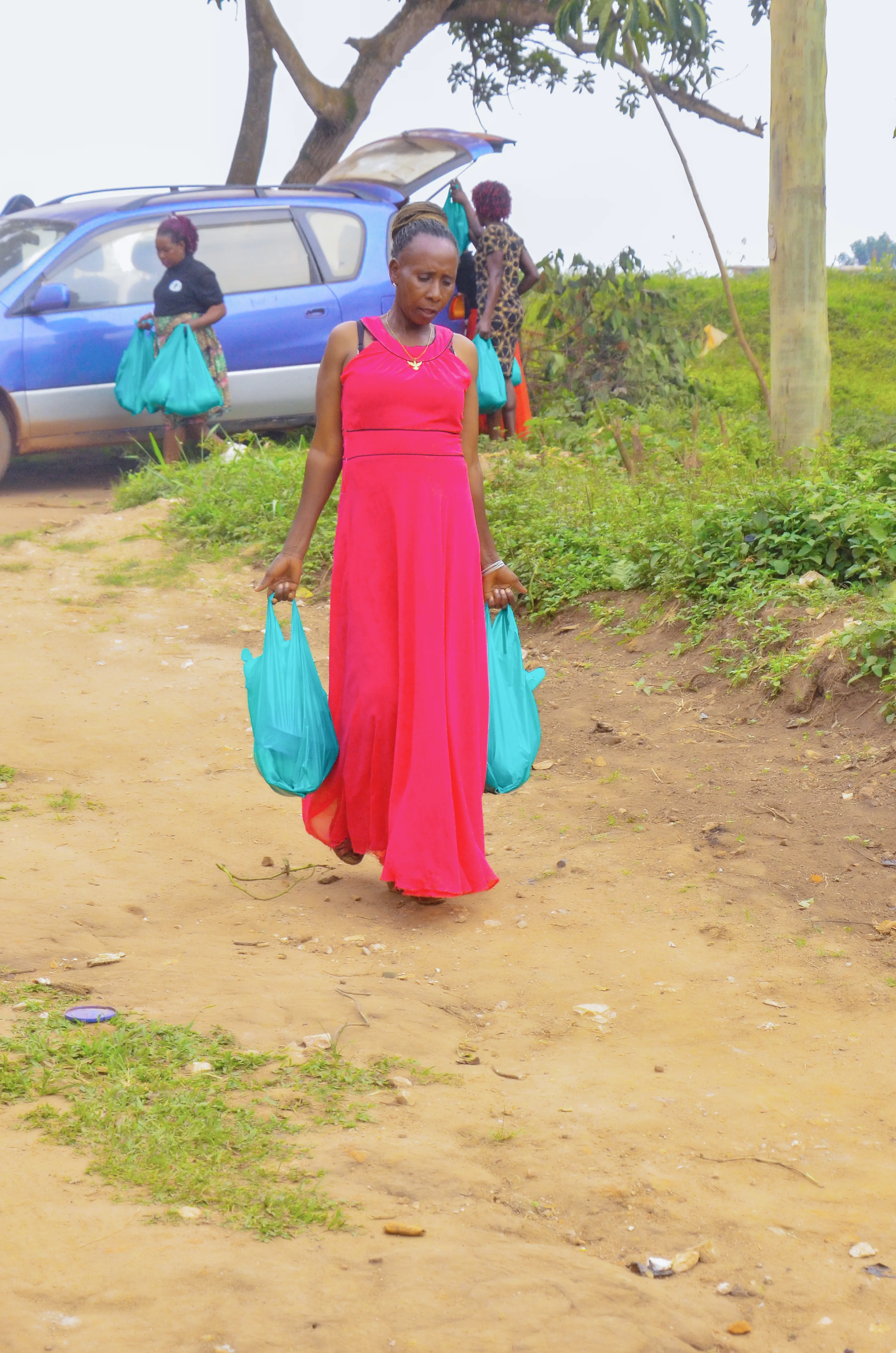 A woman in a red dress carrying two supply bags along a path